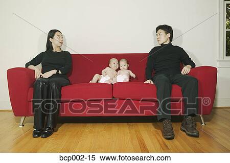 Stock Photography - Parents sitting on a sofa with twin babies.. Fotosearch