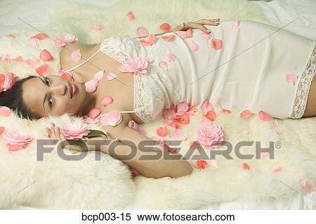 Stock Photography - A woman resting on a bed strewn with flowers.. Fotosearch