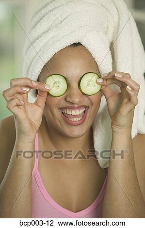 Stock Image - Woman holding cucumber slices over both eyes.. Fotosearch