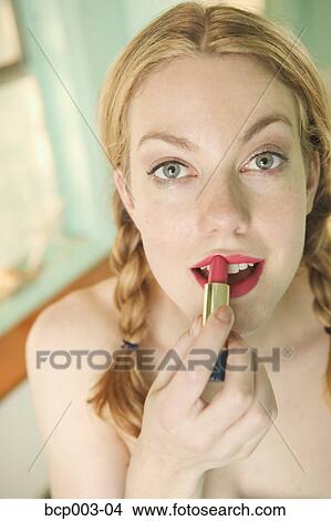Picture - Young woman applying red lipstick.. Fotosearch