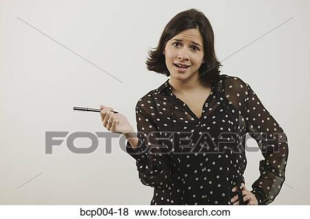 Stock Photo - Studio portrait of young woman, 20s, holding out a pen, hand on hip. . Fotosearch