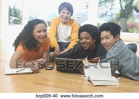 Stock Image - Four teenage kids working on a laptop and school books. . Fotosearch