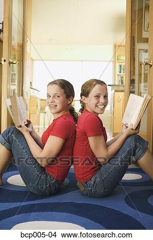 Teenage girls sitting back to back and holding books. View Large Photo Image Picture - Teenage girls sitting back to back and holding books.. Fotosearch