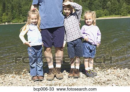 Stock Image - Three children standing with their father by a lake.. Fotosearch