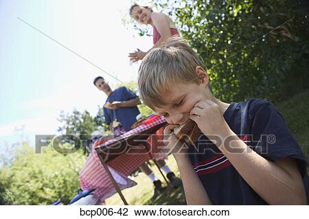Young boy eating at a family picnic. View Large Photo Image Stock Image - Young boy eating at a family picnic.. Fotosearch