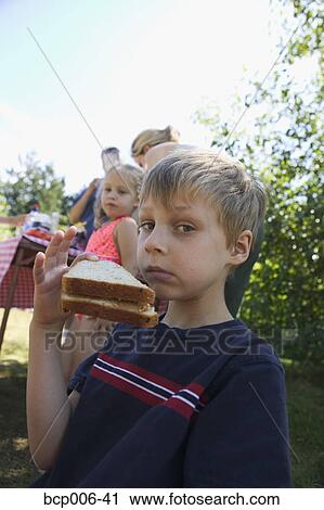 Stock Image - Young boy eating with family at a picnic.. Fotosearch