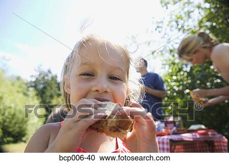 Stock Image - Young girl eating sandwich at a campsite picnic.. Fotosearch