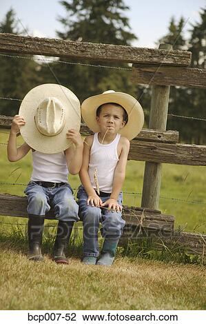 Stock Image - Twin boys in cowboy hats sitting on a fence.. Fotosearch