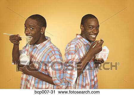 Stock Image - Twin teenage African-American boys eating noodles from cartons.. Fotosearch