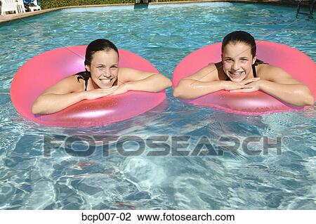 Twin teenage girls float side by side in a swimming pool. View Large Photo Image Stock Image - Twin teenage girls float side by side in a swimming pool.. Fotosearch