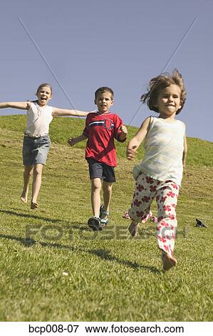 Stock Photo - Three young siblings running down a grassy hill.. Fotosearch