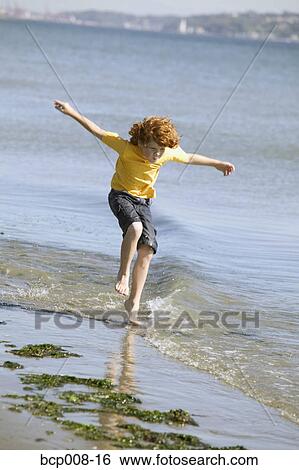 Young boy hopping in water on a beach. View Large Photo Image Stock Photograph - Young boy hopping in water on a beach.. Fotosearch