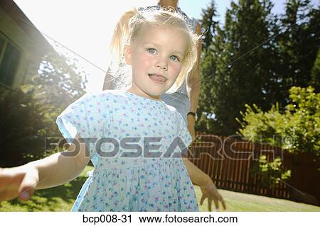 Stock Image - Young girl outdoors with an adult behind her.. Fotosearch