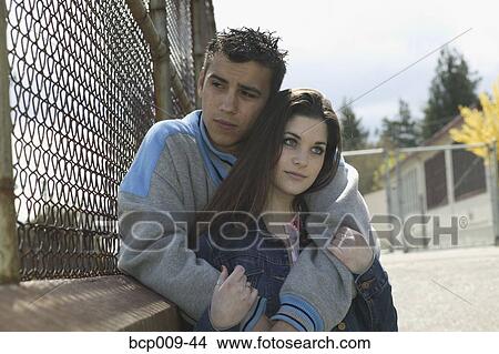Caucasian teen couple pause by a schoolyard fence. View Large Photo Image Picture - Caucasian teen couple pause by a schoolyard fence.. Fotosearch