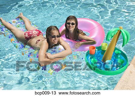 Stock Image - Two teenage girls lounging in a swimming pool.. Fotosearch