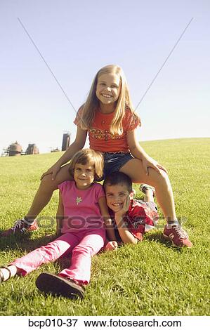 Stock Photo - Three siblings on a grassy hillside.. Fotosearch