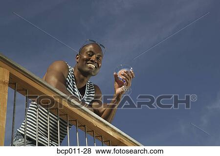 Man leaning on a rail, holding a drink. View Large Photo Image Stock Photo - Man leaning on a rail, holding a drink.. Fotosearch