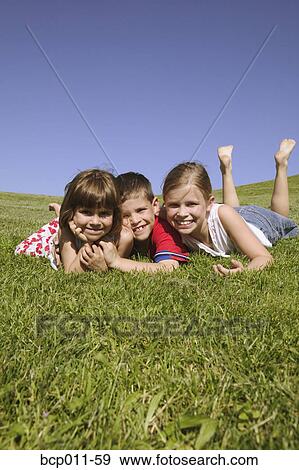 Stock Photo - Three children lying on grassy hillside.. Fotosearch
