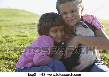 Stock Image - Two girls hugging their dog.. Fotosearch