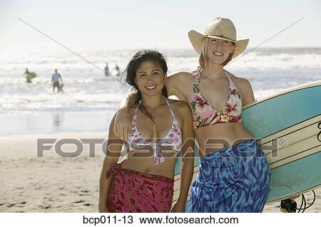 Two women at the beach with a surfboard. View Large Photo Image Stock Image - Two women at the beach with a surfboard.. Fotosearch