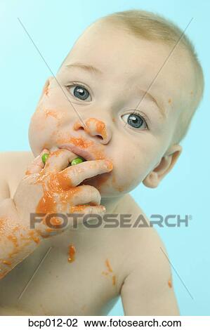 Stock Image - Infant eating baby food with fingers.. Fotosearch