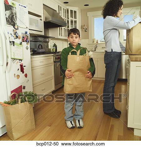Stock Image - Mother and son unloading groceries in the kitchen. . Fotosearch