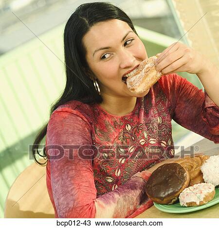 Stock Image - Young woman eating a doughnut.. Fotosearch