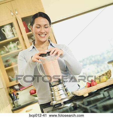 Stock Image - Young woman preparing a smoothie in a blender.. Fotosearch