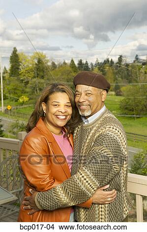 Picture - A couple hugging on the porch of their home.. Fotosearch