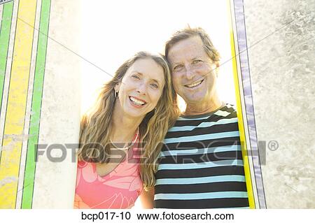 Stock Image - A couple standing between surfboards.. Fotosearch