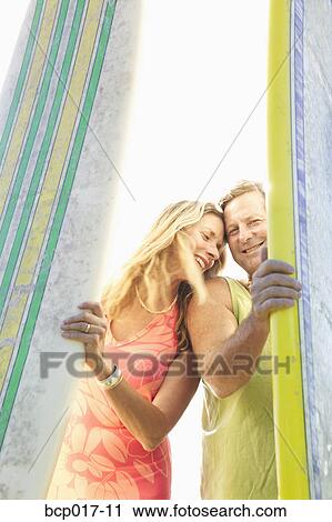 Stock Image - A couple standing between surfboards.. Fotosearch