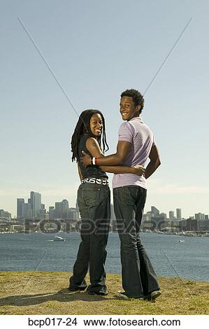 A couple standing together on a hill overlooking a lake and skyline. View Large Photo Image Picture - A couple standing together on a hill overlooking a lake and skyline.. Fotosearch