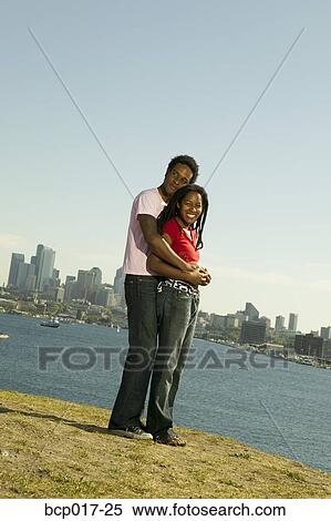 A couple standing together on a hill overlooking a lake and skyline. View Large Photo Image Stock Photography - A couple standing together on a hill overlooking a lake and skyline.. Fotosearch