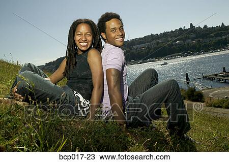 A young couple sitting back-to-back by a lake. View Large Photo Image Stock Image - A young couple sitting back-to-back by a lake.. Fotosearch