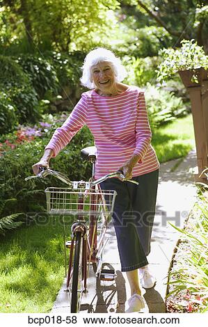 Stock Photo - A senior woman walking her bicycle.. Fotosearch
