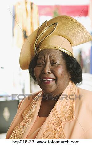 Stock Image - A senior woman wearing a yellow dress and hat.. Fotosearch
