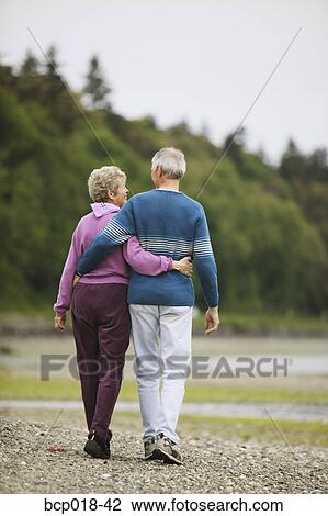 Couple walking on the beach with their arms around each other. View Large Photo Image Stock Image - Couple walking on the beach with their arms around each other.. Fotosearch