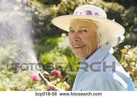 Stock Photograph - Senior woman watering her garden.. Fotosearch