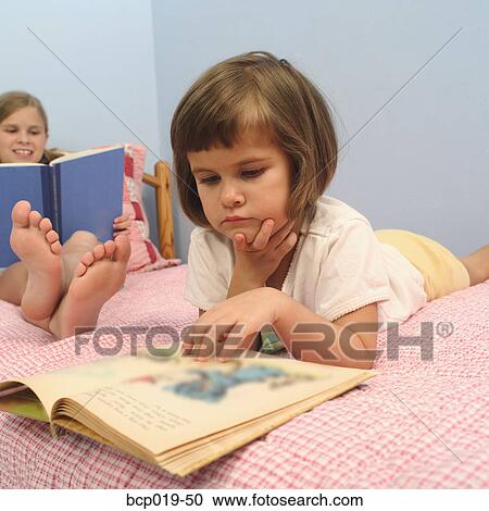 Young girls reading on a bed. View Large Photo Image Stock Image - Young girls reading on a bed.. Fotosearch