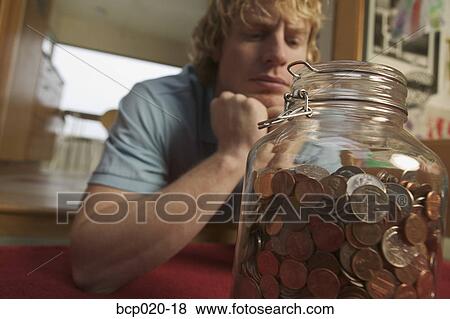 A young man contemplating a jar full of coins. View Large Photo Image Stock Photo - A young man contemplating a jar full of coins.. Fotosearch