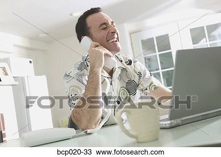 Man talking on the phone and working on a laptop. View Large Photo Image Stock Image - Man talking on the phone and working on a laptop.. Fotosearch