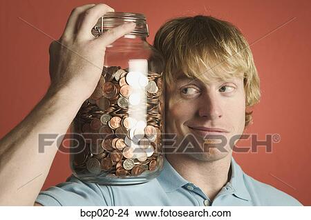 Young man eyeballing a large glass coin jar on his shoulder. View Large Photo Image Picture - Young man eyeballing a large glass coin jar on his shoulder.. Fotosearch