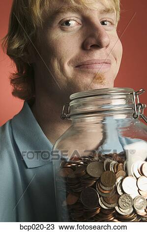 Young man holding a large glass coin jar. View Large Photo Image Stock Image - Young man holding a large glass coin jar.. Fotosearch