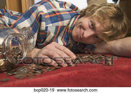 Young man playing with a pile of coins spilled from a coin jar. View Large Photo Image Stock Photo - Young man playing with a pile of coins spilled from a coin jar.. Fotosearch