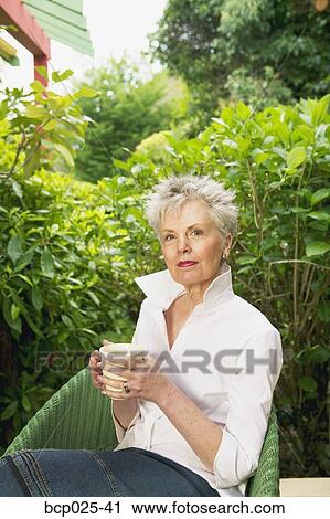 A middle-aged woman sitting and holding a cup View Large Photo Image Stock Image - A middle-aged woman sitting and holding a cup. Fotosearch