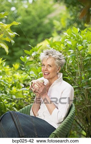 A middle-aged woman sitting and holding a cup View Large Photo Image Stock Image - A middle-aged woman sitting and holding a cup. Fotosearch
