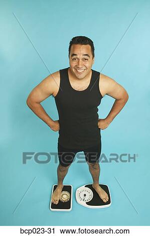 Stock Image - A happy man standing on scales. Fotosearch