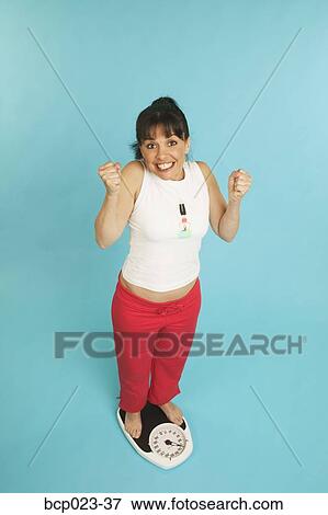 A happy woman standing on a scale View Large Photo Image Stock Photo - A happy woman standing on a scale. Fotosearch