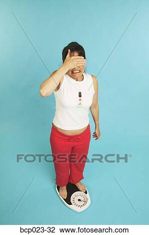 Stock Image - A very unhappy woman standing on a scale. Fotosearch