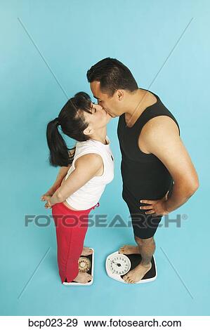Couple kissing while standing on scales View Large Photo Image Stock Photo - Couple kissing while standing on scales. Fotosearch